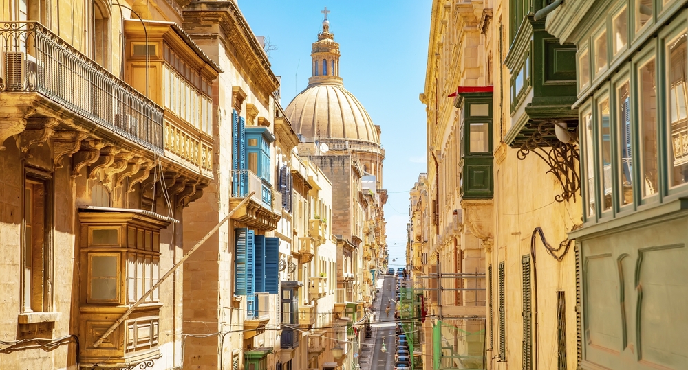 Sonnige Straße in der Altstadt von Valletta, Basilika Unserer Lieben Frau vom Berg Karmel auf einem Hintergrund, Malta, Valletta