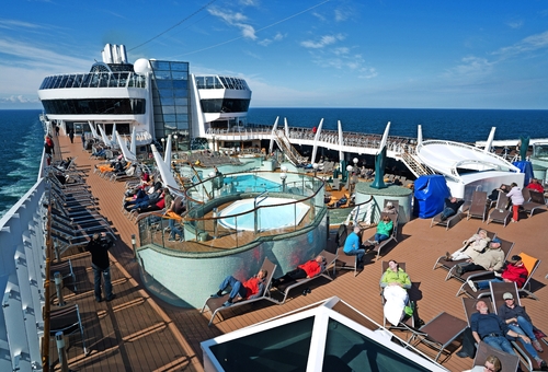 Menschen entspannen auf einem Kreuzfahrtschiffdeck mit Pool und Sonnenliegen.